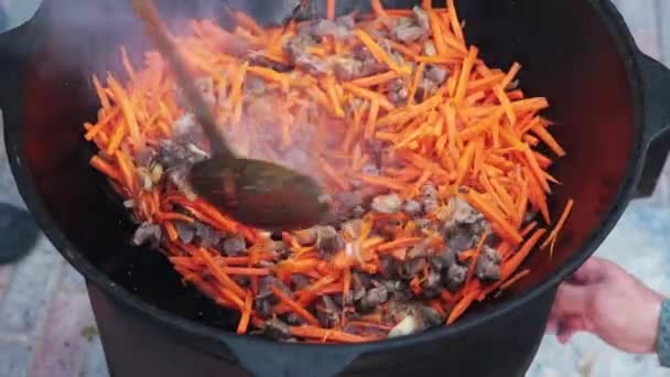 Oezbeekse nationale gerecht Pilaf in een grote gietijzeren ketel op het vuur, voeg gesneden rode wortelen, rijst, lam, schapenvlees vet, de dikke staart, sesamolie, ui, knoflook, rode hete Chili peper — Stockvideo