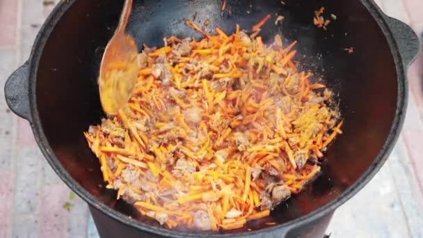 Uzbecká národní miska pilaf ve velkém litinové kotlíku na ohni, posypané soli, kmínkové semena, zrzavá mrkev, rýže, jehněčí, skopové, mléčný ocas, sezamový olej, cibuli, česnek, červený horký chilli papriček — Stock video
