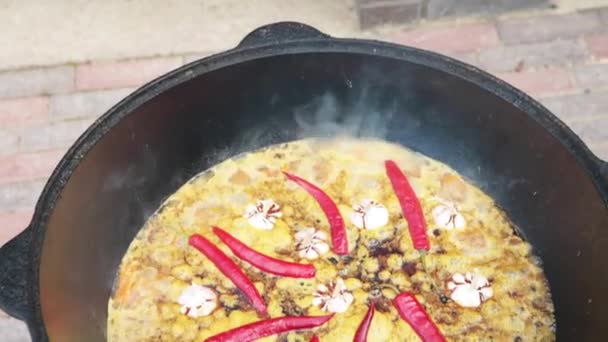 Plato nacional uzbeko pilaf en un gran caldero de hierro fundido en el fuego, zanahorias rojas en rodajas, agua fría, añadir todo el ajo y chiles rojos, comienza a hervir, arroz, cordero, grasa de cordero, la cola de grasa — Vídeo de stock