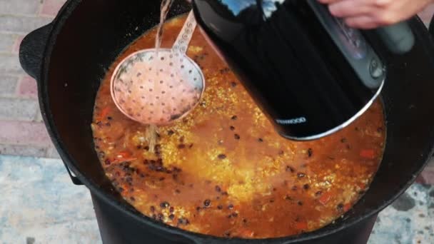 Uzbek national dish pilaf in a large cast-iron cauldron on the fire, added hot water, sliced red carrots, added barberry, garlic, red chili, added rice, lamb, mutton fat, the fat tail, sesame oil — Stock Video