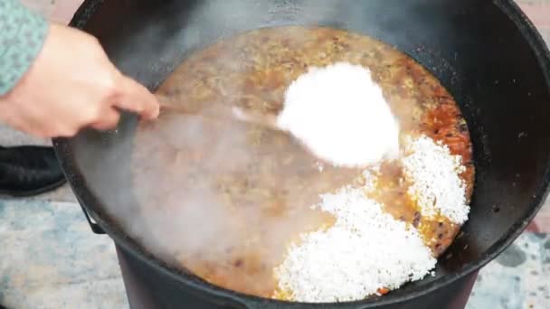 Pilaf plato nacional uzbeko en un gran caldero de hierro fundido en el fuego, zanahorias rojas en rodajas, agracejo añadido, ajo se retira y chile rojo, arroz añadido, cordero, grasa de cordero, la cola de grasa, aceite de sésamo — Vídeos de Stock