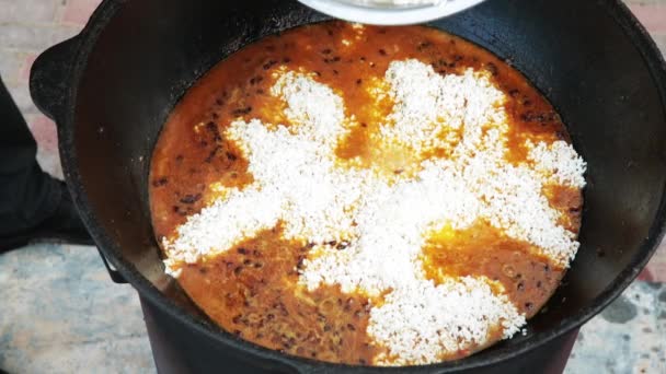 Pilaf plato nacional uzbeko en un gran caldero de hierro fundido en el fuego, zanahorias rojas en rodajas, agracejo añadido, ajo se retira y chile rojo, arroz añadido, cordero, grasa de cordero, la cola de grasa, aceite de sésamo — Vídeo de stock