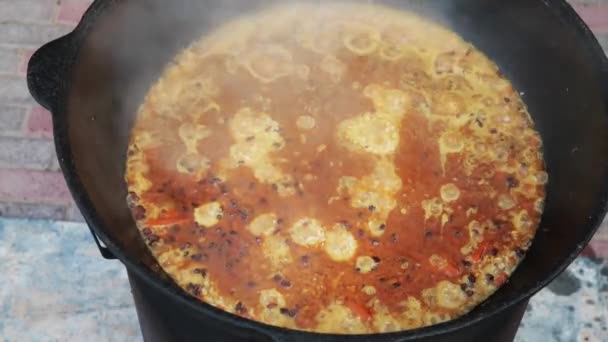 Uzbek national dish pilaf in a large cast-iron cauldron on the fire, added hot water, sliced red carrots, added barberry, garlic, red chili, added rice, lamb, mutton fat, the fat tail, sesame oil — Stock Video