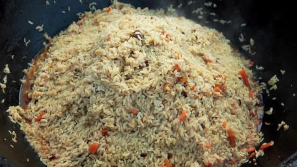 Usbekisches Nationalgericht pilaf in einem großen gusseisernen Kessel auf dem Feuer, gemischtes fertiges pilaf, in Scheiben geschnittene rote Karotte, Berberitze, Knoblauchlöcher, rote Chilischote, Reis, Lamm, Hammelfett, der Fettschwanz, Sesamöl — Stockvideo