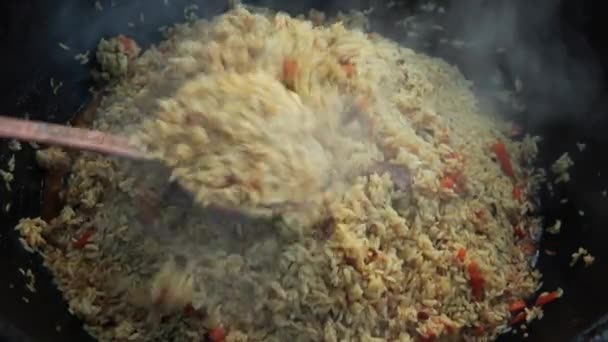 Usbekisches Nationalgericht pilaf in einem großen gusseisernen Kessel auf dem Feuer, gemischtes fertiges pilaf, in Scheiben geschnittene rote Karotte, Berberitze, Knoblauchlöcher, rote Chilischote, Reis, Lamm, Hammelfett, der Fettschwanz, Sesamöl — Stockvideo