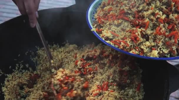 Uzbecká národní miska pilaf ve velkém litinovém kotlíku na ohni, roztáhl pilaf na velkém talíři, mrkev, Barberry, česnekový tuk, papriku z chilli, rýži, jehněčí, skopové maso, tlustý ocas, sezamový olej — Stock video