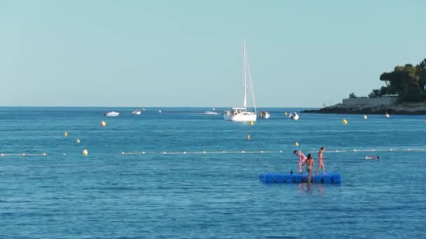 França, Menton, 2015.08.27: Praia Menton, Roquebrune Cap Martin, Provence Alpes Cote dAzur, água azul, banho muitas crianças em pontão de plástico, iates no fundo, barco à vela — Vídeo de Stock