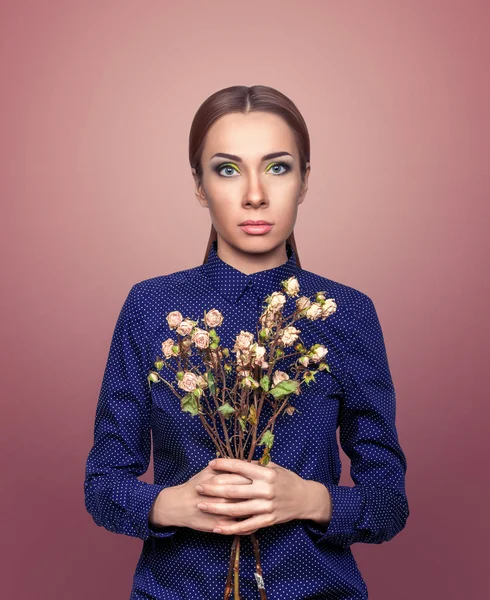 Chica con un ramo de rosas marchitas sobre un fondo rosa — Foto de Stock