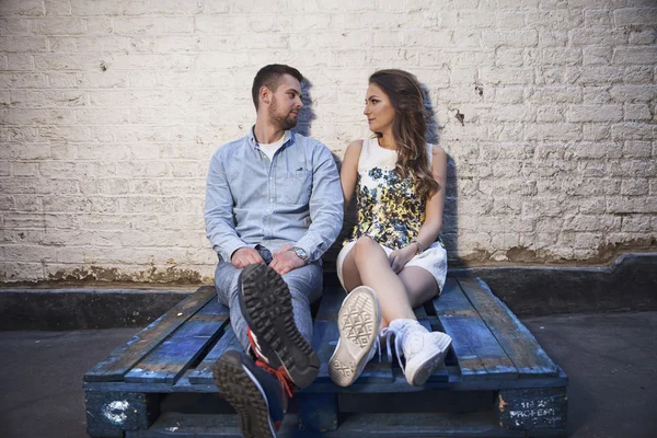 Giovane coppia seduta su un pallet contro muro di mattoni — Foto Stock