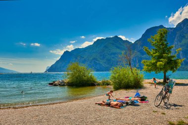 Riva del Garda, Lago di Garda, İtalya - 12 Haziran 2020: Yaz mevsiminde Garda Gölü 'nde güneşlenmek ve güneşlenmek için sahilde oturanlar