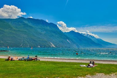 Riva del Garda, Lago di Garda, İtalya - 12 Haziran 2020: Yaz mevsiminde Garda Gölü 'nde güneşlenmek ve güneşlenmek için sahilde oturanlar