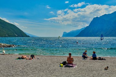 Riva del Garda, Lago di Garda, İtalya - 12 Haziran 2020: Yaz mevsiminde Garda Gölü 'nde güneşlenmek ve güneşlenmek için sahilde oturanlar