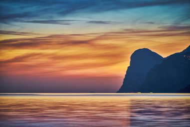 Güzel Garda Gölü 'nün dağlarla çevrili görüntüsü, Garda Gölü' nde gün batımının manzarası, güzel günbatımı renkleri, İtalya, uzun pozlardan dolayı yumuşak odak