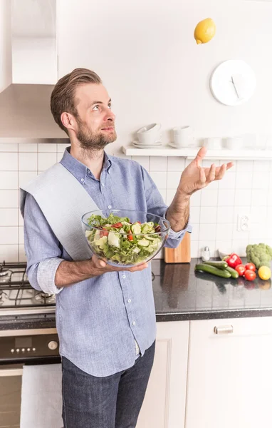 Feliz hombre sonriente con una ensalada de verduras frescas en la cocina — Foto de Stock