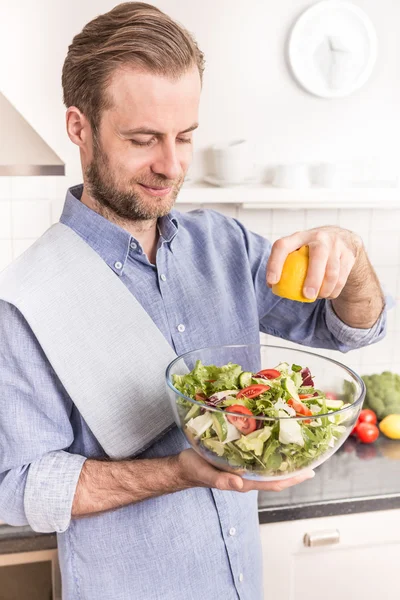 Glücklich lächelnder Mann, der in der Küche frischen Gemüsesalat zubereitet — Stockfoto