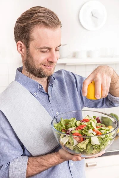 Feliz hombre sonriente haciendo ensalada de verduras frescas en la cocina — Foto de Stock