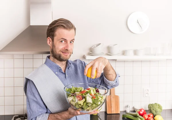 Feliz homem sorrindo fazendo salada de legumes frescos na cozinha — Fotografia de Stock