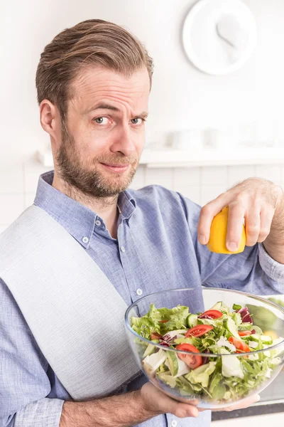 Feliz hombre sonriente haciendo ensalada de verduras frescas en la cocina —  Fotos de Stock