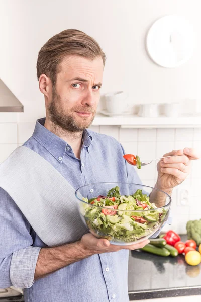 Mann isst frischen Gemüsesalat in der Küche — Stockfoto