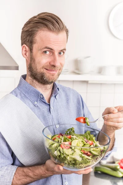 Feliz hombre sonriente comiendo ensalada de verduras frescas en la cocina —  Fotos de Stock