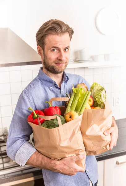 Homem feliz segurando sacos de compras de supermercado de papel na cozinha — Fotografia de Stock