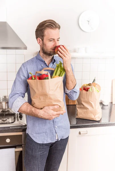 Homem feliz segurando saco de compras de papel na cozinha — Fotografia de Stock