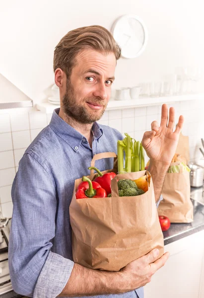 Щасливий чоловік тримає паперовий продуктовий сумку на кухні — стокове фото