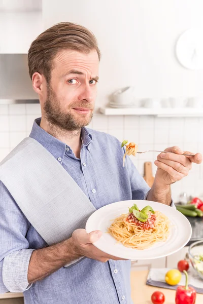 Happy smiling man eating spaghetti bolognese in the kitchen — Stock Photo, Image