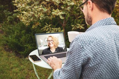 Erkek (iş adamı) bahçede otururken bir iş arkadaşıyla dizüstü bilgisayarda görüntülü konuşma yapıyor. İş ve teknoloji - telekomünikasyon veya uzaktan çalışma.