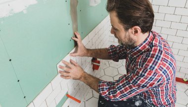 Caucasian interior finishing worker (tiler) laying small white ceramic tiles on the wall. Bathroom renovation works. Handyman in plaid shirt. clipart