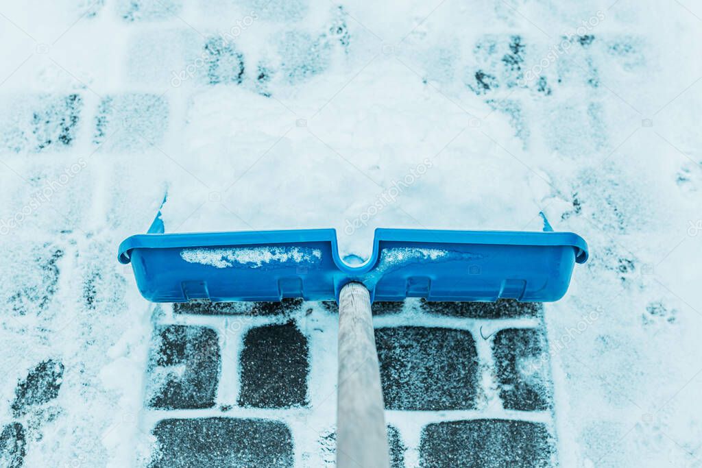 Cold snowy winter - blue shovel removing snow from the paver path (sidewalk) outdoor.