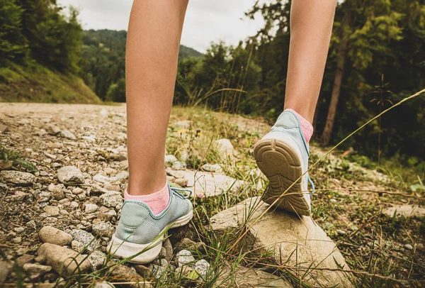Recreation - hiking among the hills. Girl legs in pastel blue sneakers on the stone path. Mountain landscape as background - active lifestyle.
