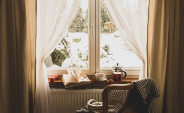 Kışın rahat bir evde rahatla. Sıcak çay, cam çaydanlık, kitap, cam kenarında bardak ve battaniye, dışarıda kar. Huzurlu kızlık zarı atmosferi, karamsar ışık, yavaş yaşam felsefesi kavramı.