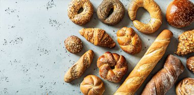 Fırın, farklı ekmek çeşitleri. Ekmek ruloları, baget, hamburgerler, çörekler ve kruvasan yukarıdan yakalanır. Boş kopya (metin) alanına sahip gri arkaplan.