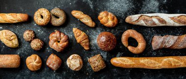 Fırın, farklı ekmek çeşitleri. Ekmek ruloları, baget, hamburgerler, çörekler ve kruvasan yukarıdan yakalanır. Siyah karatahta arkaplan, yatay afiş düzeni.