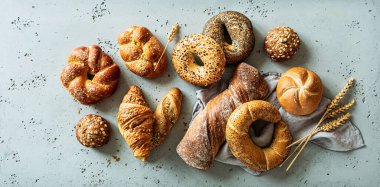 Fırın, çeşitli ekmek çeşitleri. Ekmek ruloları, bagel, tatlı çörek ve kruvasan yukarıdan yakalanır (düz yatak). Gri taş arka plan.