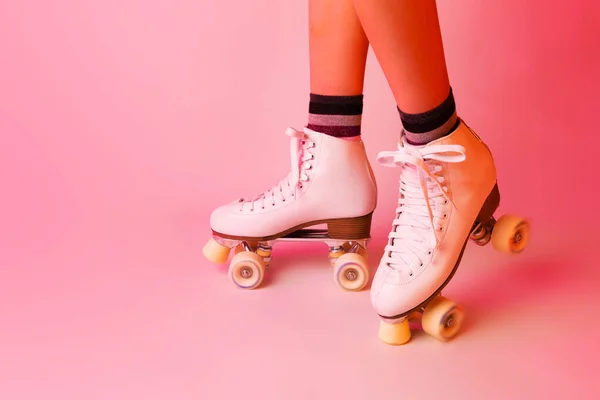 Sports equipment and recreation - classic white leather roller skates and girls legs. Pastel pink background. Layout with free copy space.