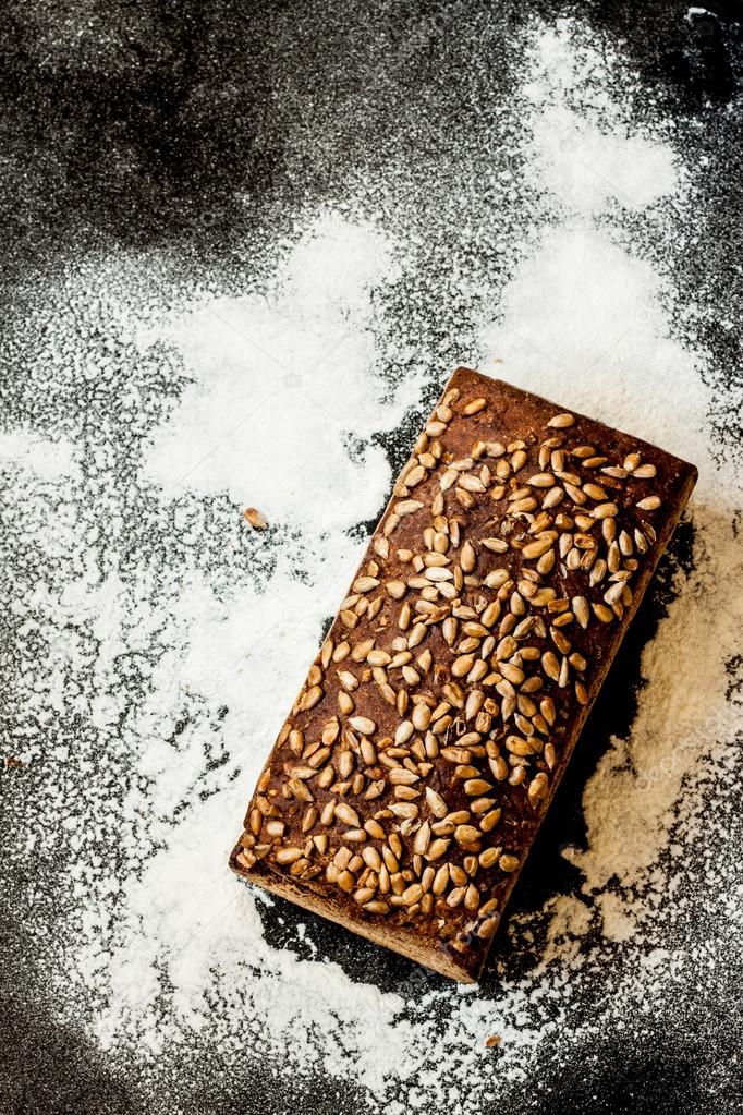 Rustic loaf of bread with sunflower seeds and flour on black chalkboard