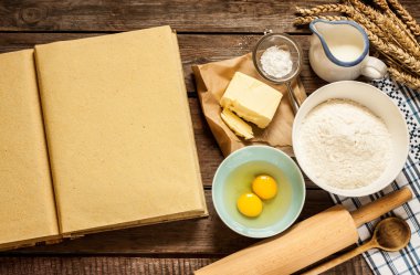 Blank cook book and baking cake ingredients on wood