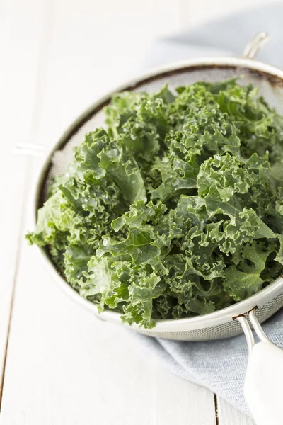 Fresh wet kale in a sieve on white planked wooden table — Stok fotoğraf