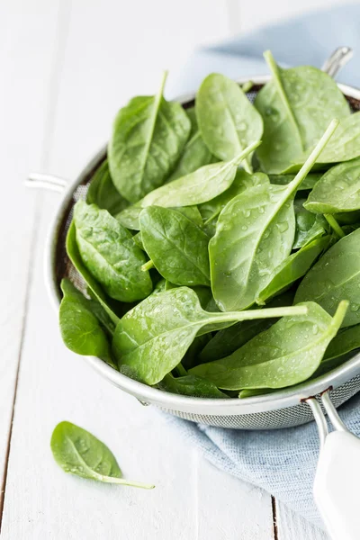 Fresh wet baby spinach leaves in a sieve on white table — ストック写真