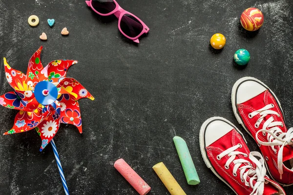Toys and red sneakers on black chalkboard - top view