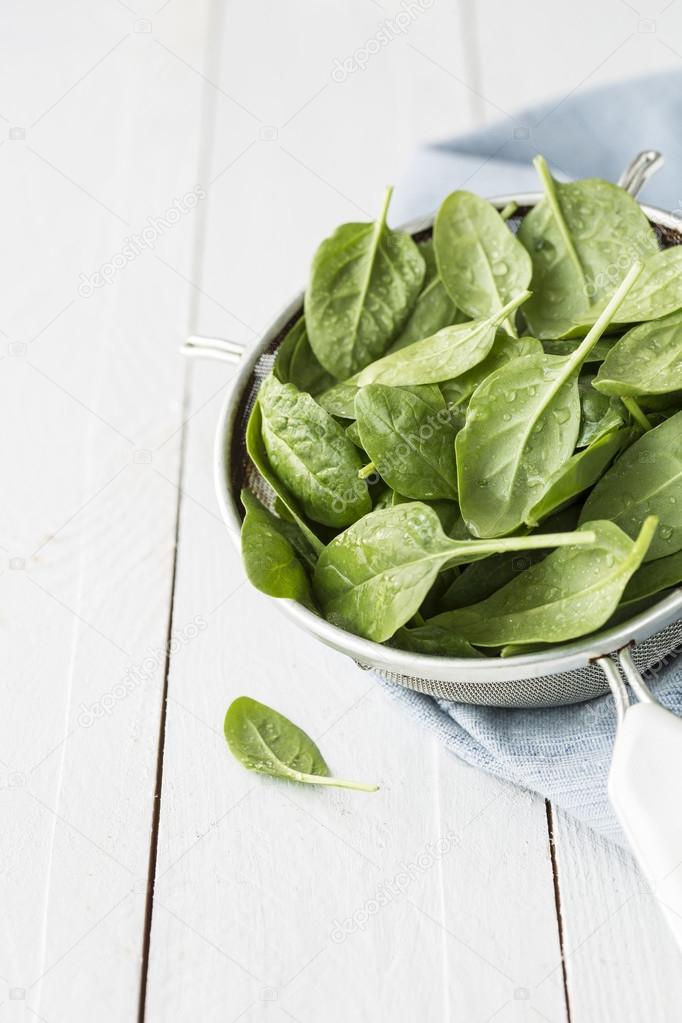 Fresh wet baby spinach leaves in a sieve on white table