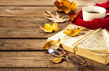 Hot coffee, vintage book, glasses and autumn leaves on wood