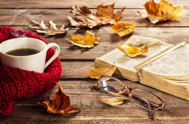 Hot coffee, vintage book, glasses and autumn leaves on wood