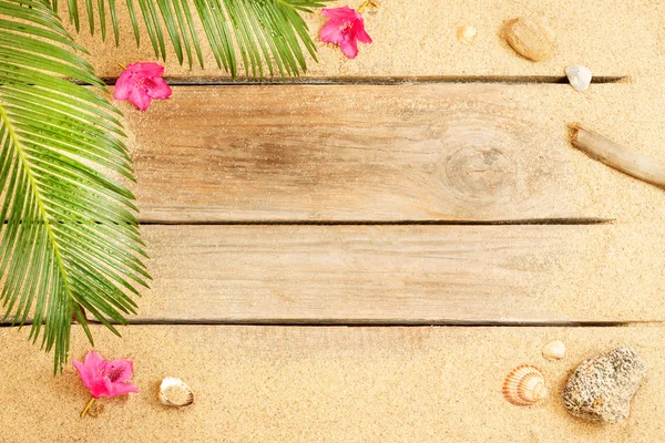 Palm tree leaves, flowers and sand on wood background