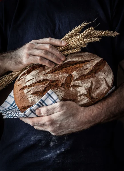 Rustic loaf of bread and wheat in man's hands — Stock Photo, Image