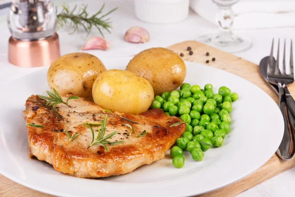 Свиная отбивная, вареная картошка и зеленый горошек подаются на блюдечке — стоковое фото