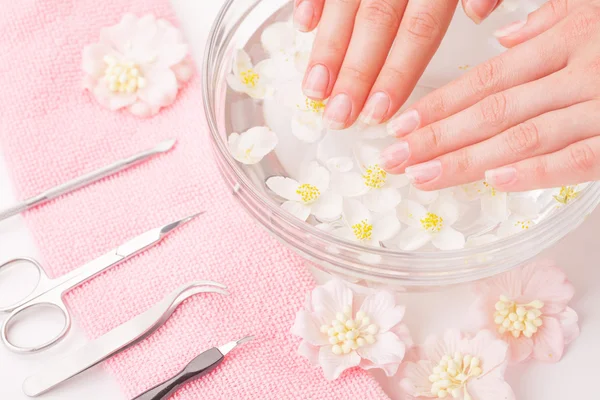 Mooie dames handen met manicure in kom met water — Stockfoto