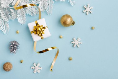 Altın yaylı beyaz hediye ve pastel mavi kağıt arka planda noel süslemeleri. Düz konum, üst görünüm, kopyalama alanı.